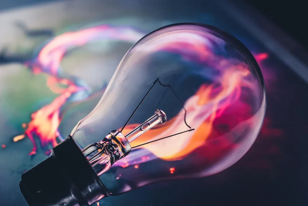 Lampadina con filamenti esposti su sfondo astratto, con vivaci colori neon che evocano un senso di creatività e innovazione.
